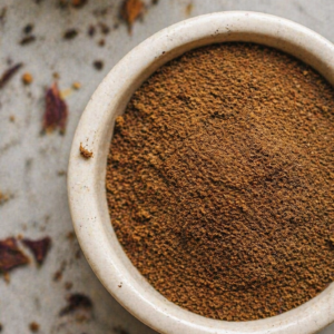 A rustic bowl filled with finely ground Blue Lotus powder used as a ceremonial extract, resting on a textured stone surface with scattered petal fragments.