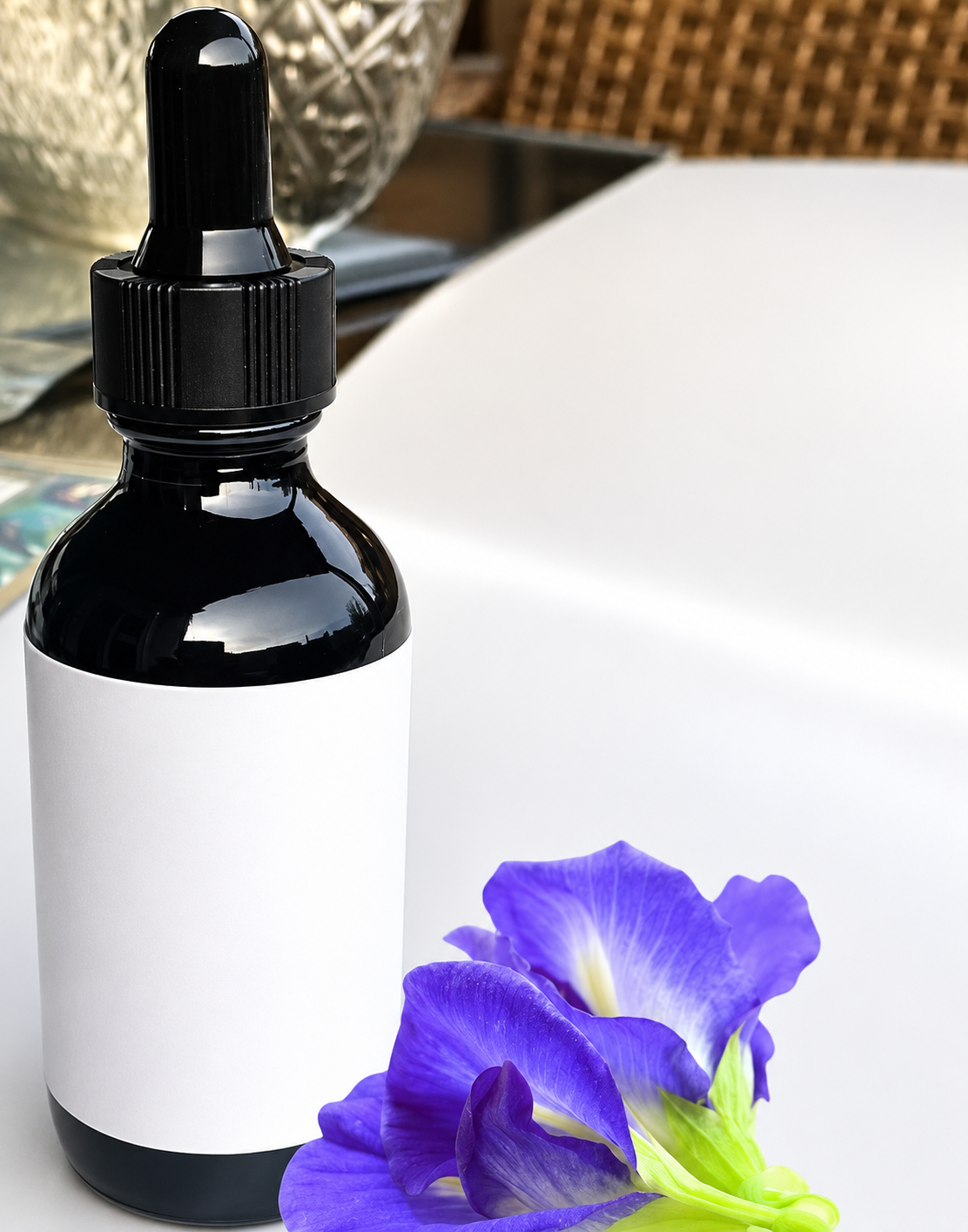 A dark glass dropper bottle containing Blue Lotus liquid ceremonial extract placed next to vibrant blue botanical flowers on a clean surface.